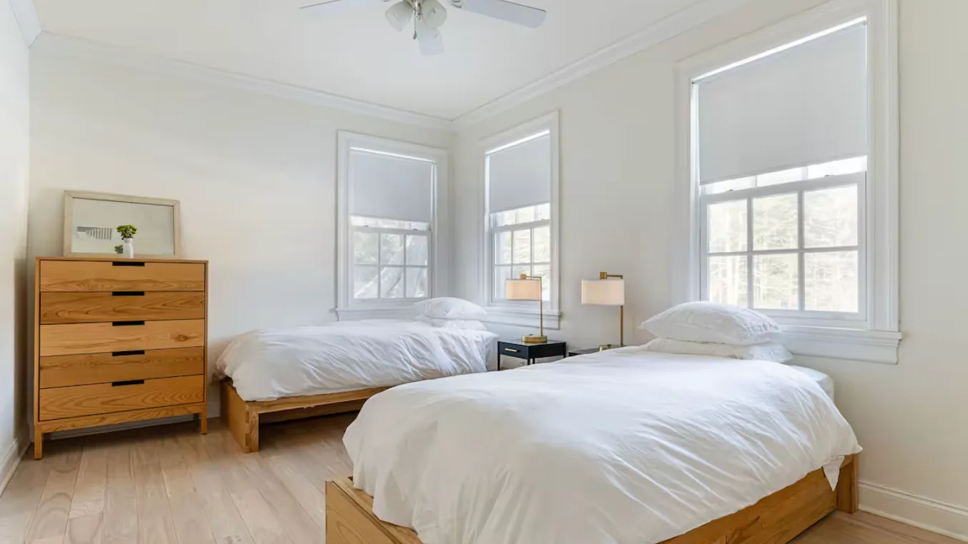 A bright bedroom with two beds and large windows.