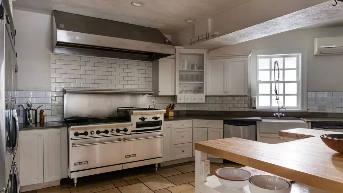 A bright kitchen with white cabinets, a range, and a large island.