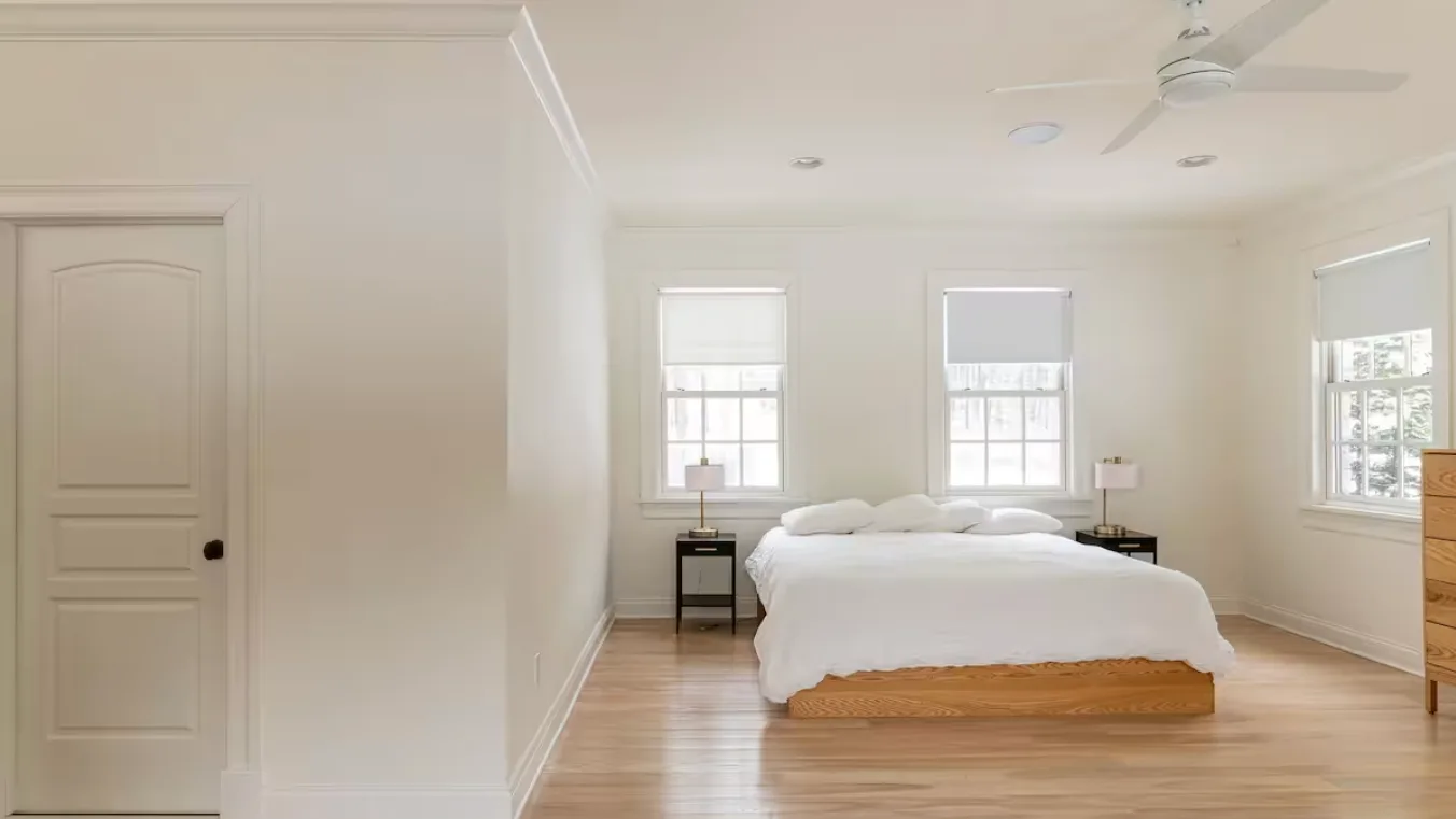 A bright bedroom with a bed centered beneath two windows.