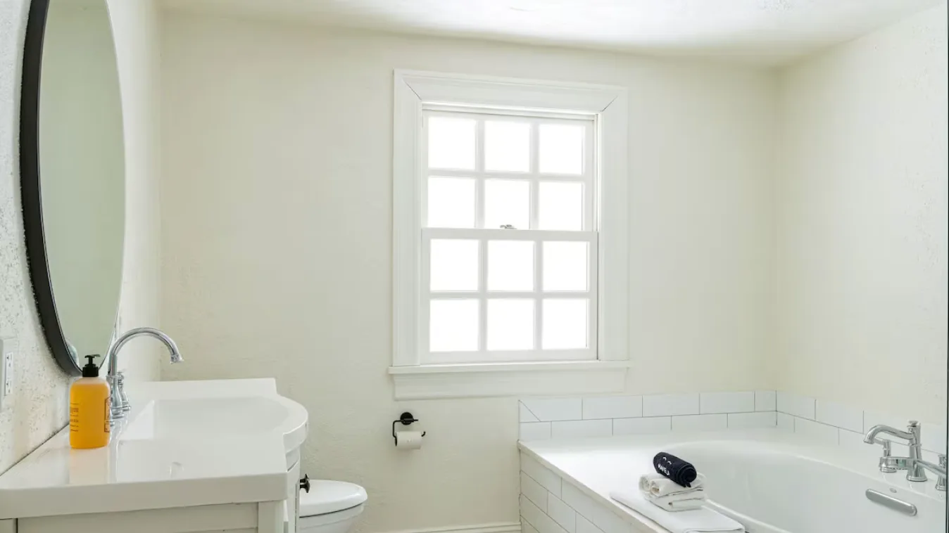 A bright bathroom with a bathtub beneath a window and a sink nearby.