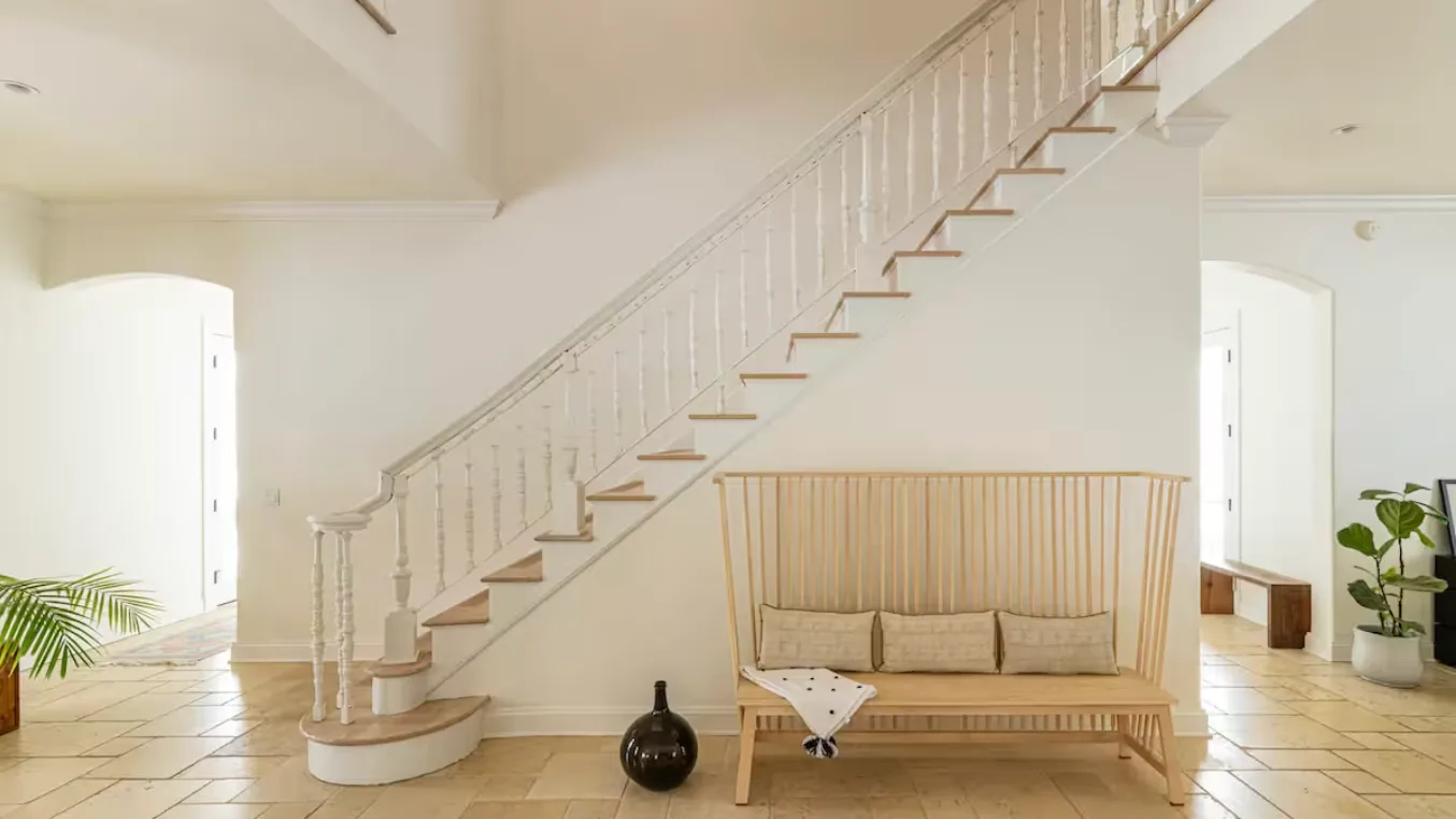 A bright interior with a staircase and a wooden bench beneath it.