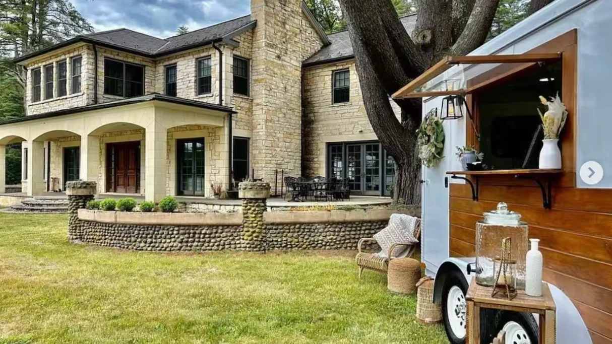 A stone house with a covered patio opens onto a lawn.