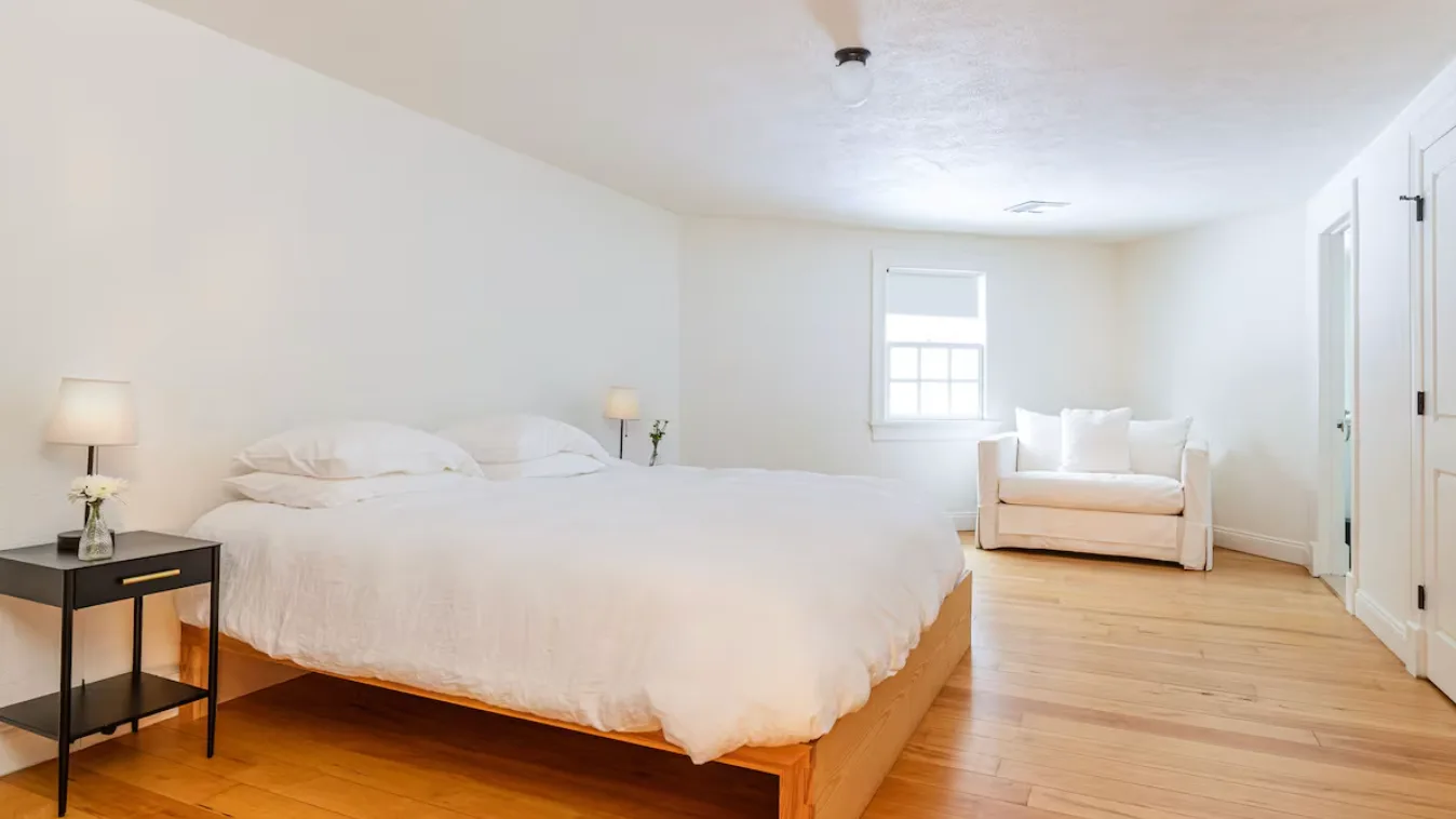 A bright bedroom with a large bed and a small seating area by the window.