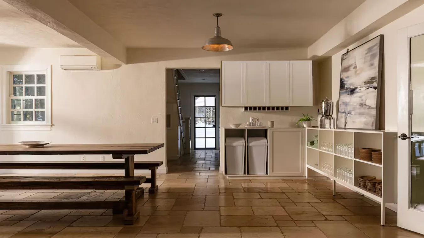A dining area with a long wooden table beside a compact kitchen.