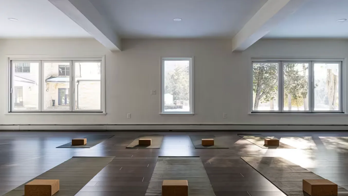 A bright room with wide windows and several mats arranged on the floor.