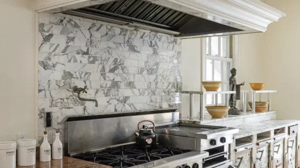 Kitchen cooking area with a wide stovetop beneath a large overhead hood.