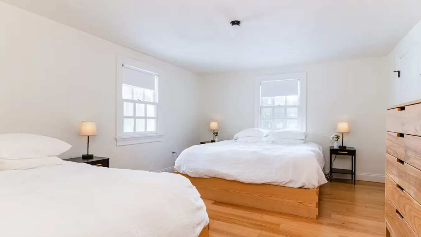A bright bedroom with two beds, bedside tables, and wooden flooring.