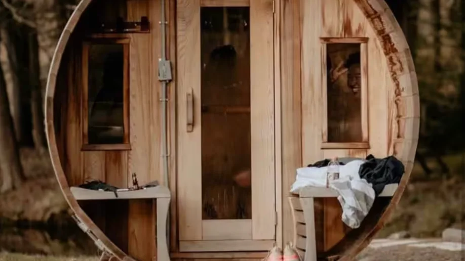 A round wooden sauna with a central glass door and small side windows.