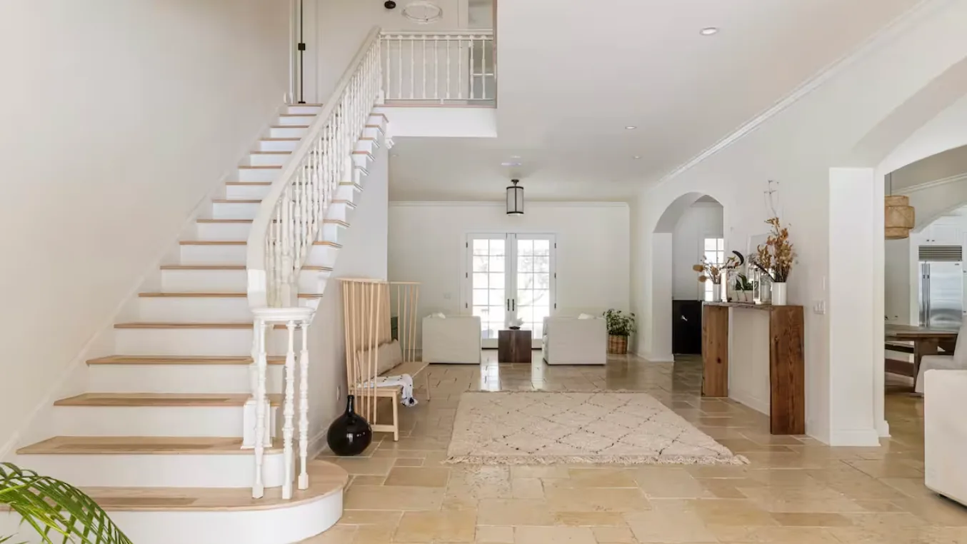 A bright living room with a staircase and a rug on the tiled floor.