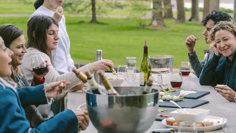 A group of people shares a meal outdoors at a table with food and drinks.