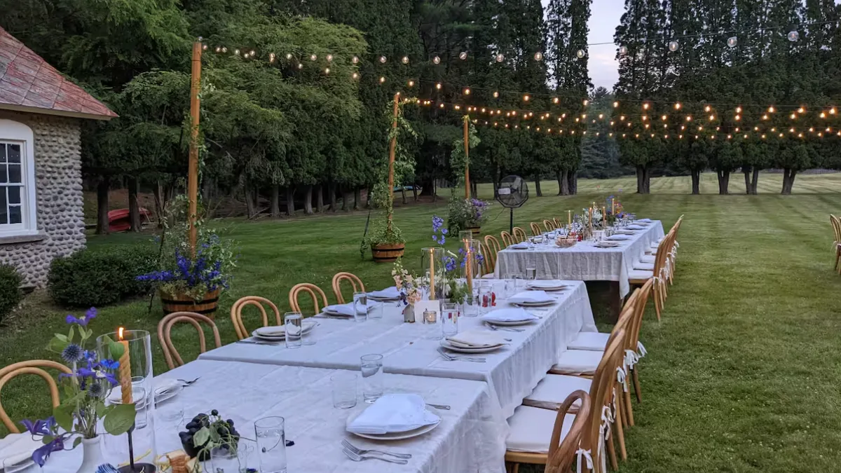 A long outdoor dining table is set on a lawn beneath string lights.