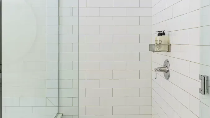 A tiled bathroom shower with a wall-mounted control and dispensers.