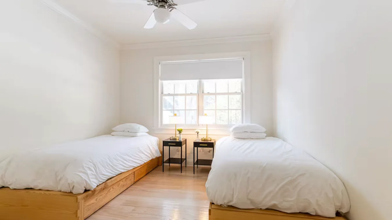 A bright bedroom with two beds beside a large window.