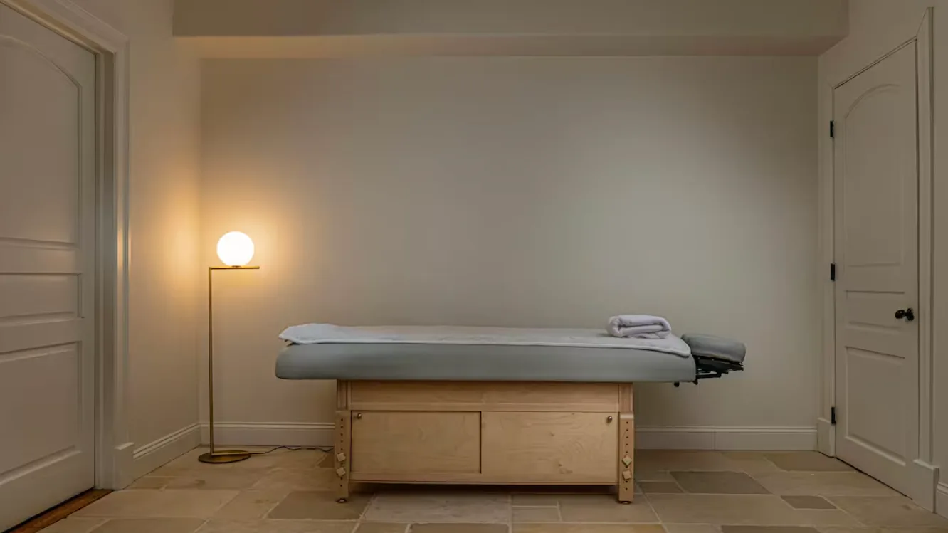 A treatment room with a padded table and a lit floor lamp.
