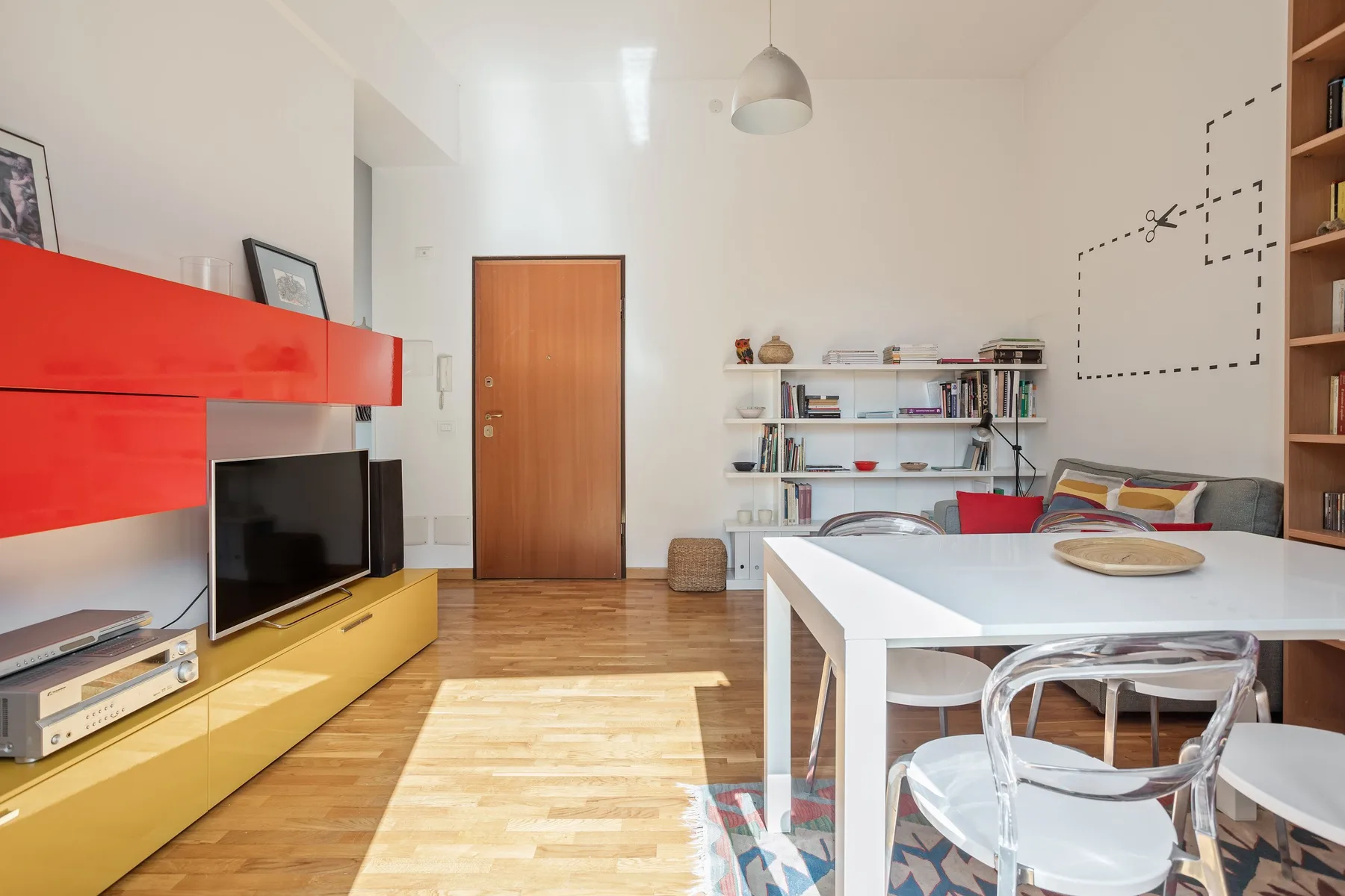 A bright living and dining area with a television, table, and open shelving.