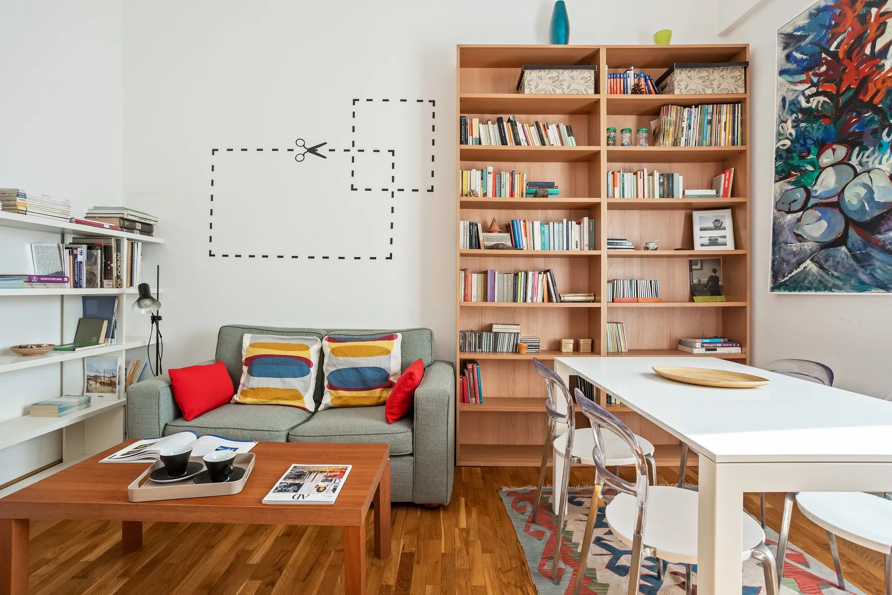 A living and dining area with a sofa, bookshelves, and a white table.