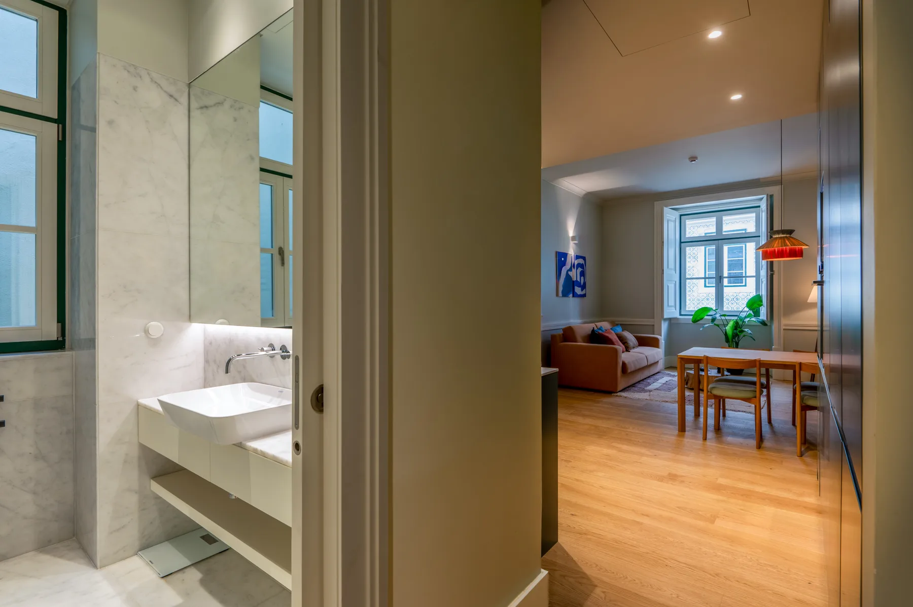 A bathroom opens onto a living and dining area with wooden flooring.