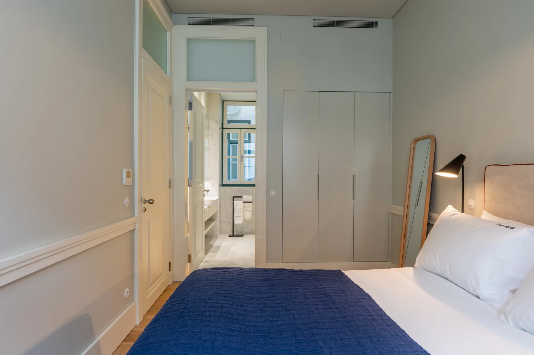 A bedroom with white bedding, a blue bedspread, and a doorway to the bathroom.