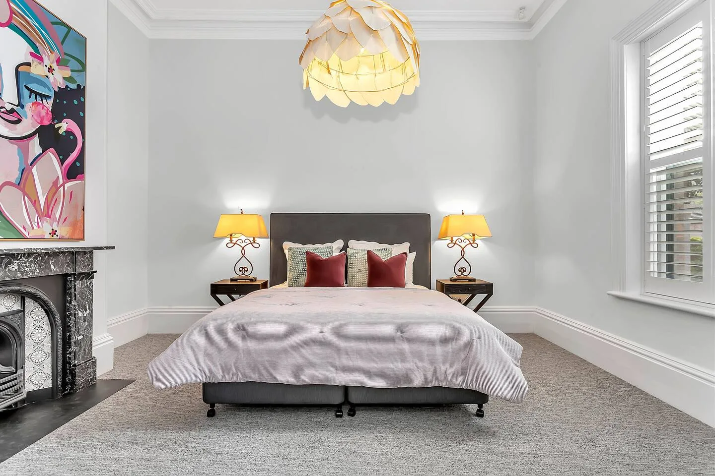 A bedroom with a centered bed, matching bedside lamps, and colorful artwork.