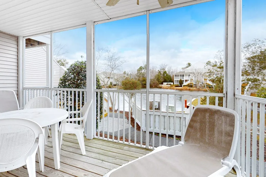 A screened porch with outdoor seating overlooks a tree-lined waterway.