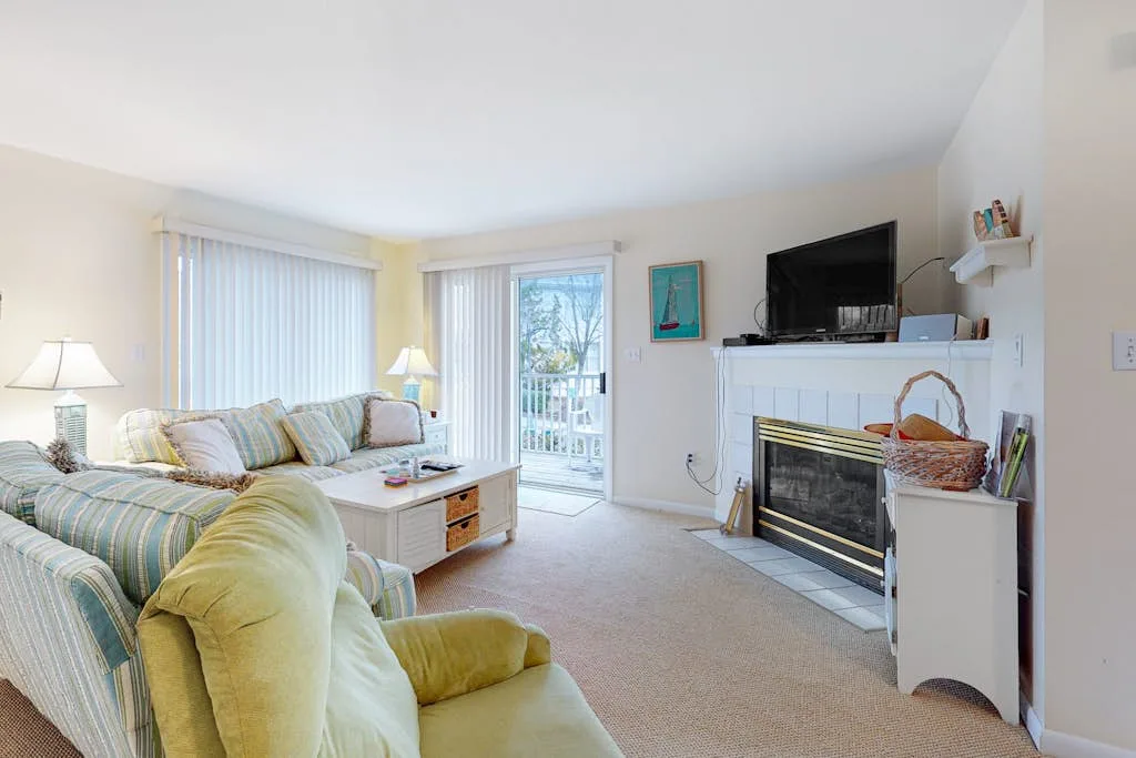 A bright living room with seating, large windows, and a fireplace.
