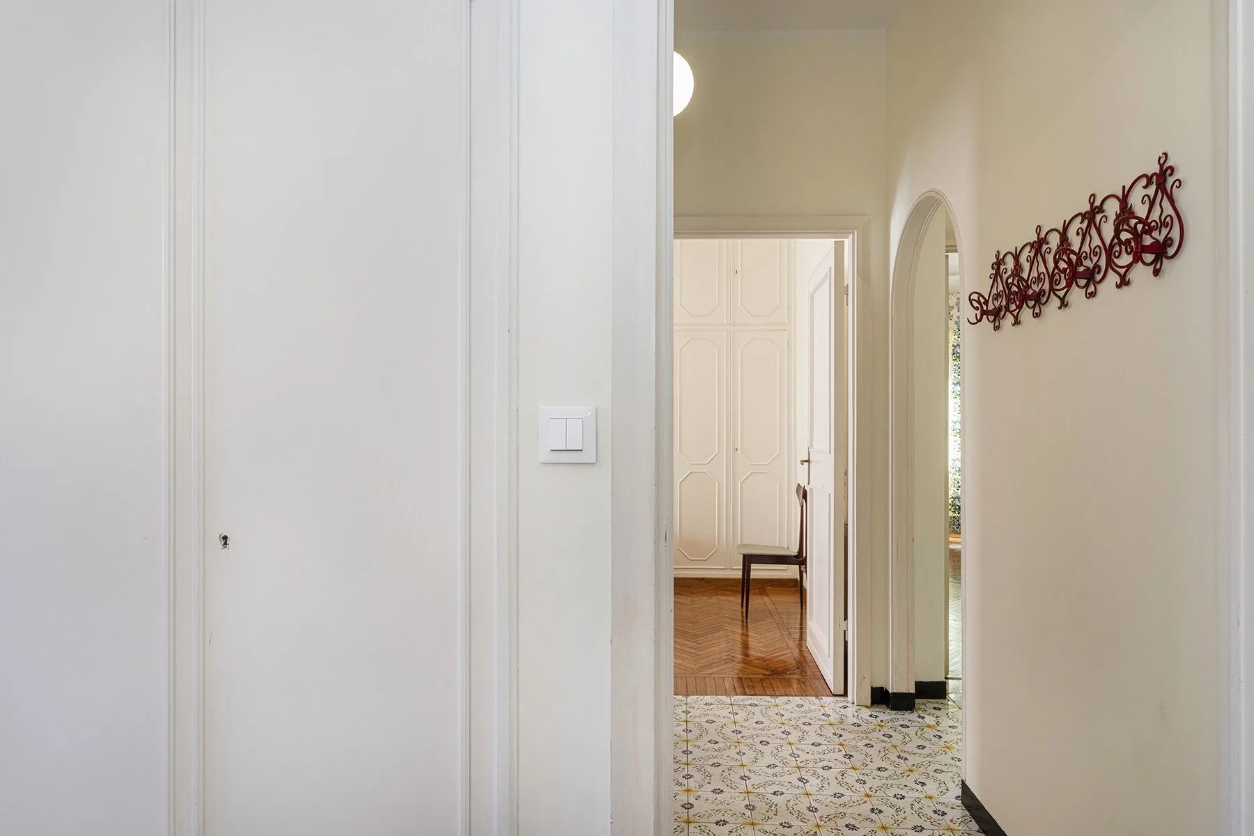 Un pasillo luminoso con suelo de baldosas estampadas y una entrada a una habitación con suelo de madera.