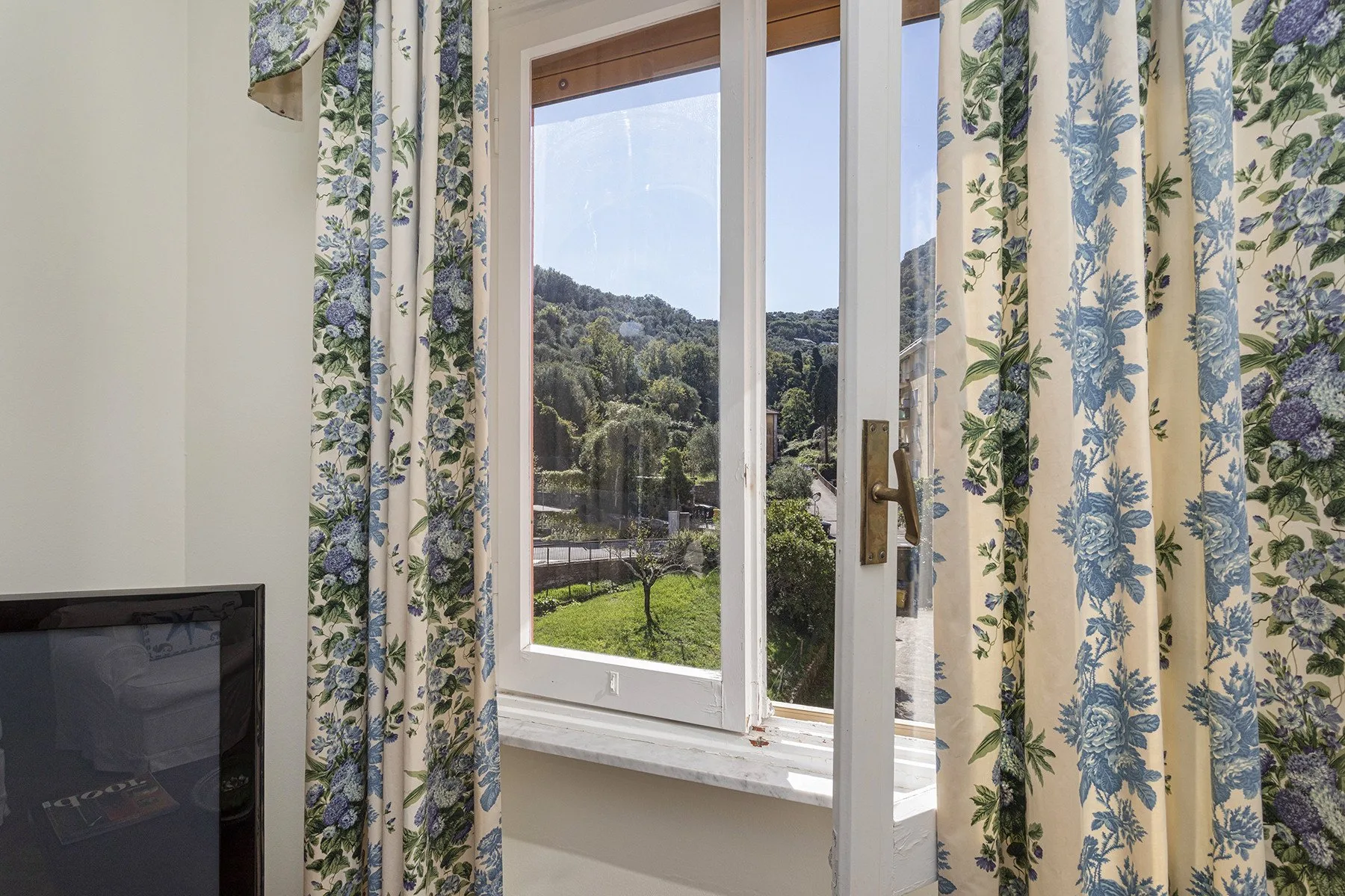 Una habitación luminosa con una ventana abierta que da a colinas verdes.