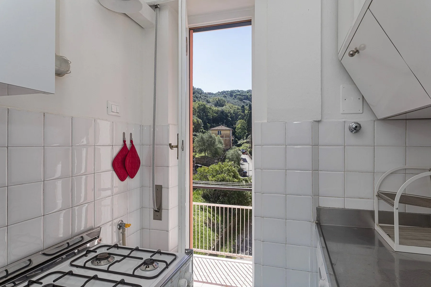 Una cocina alicatada da a un balcón con vistas a colinas verdes.