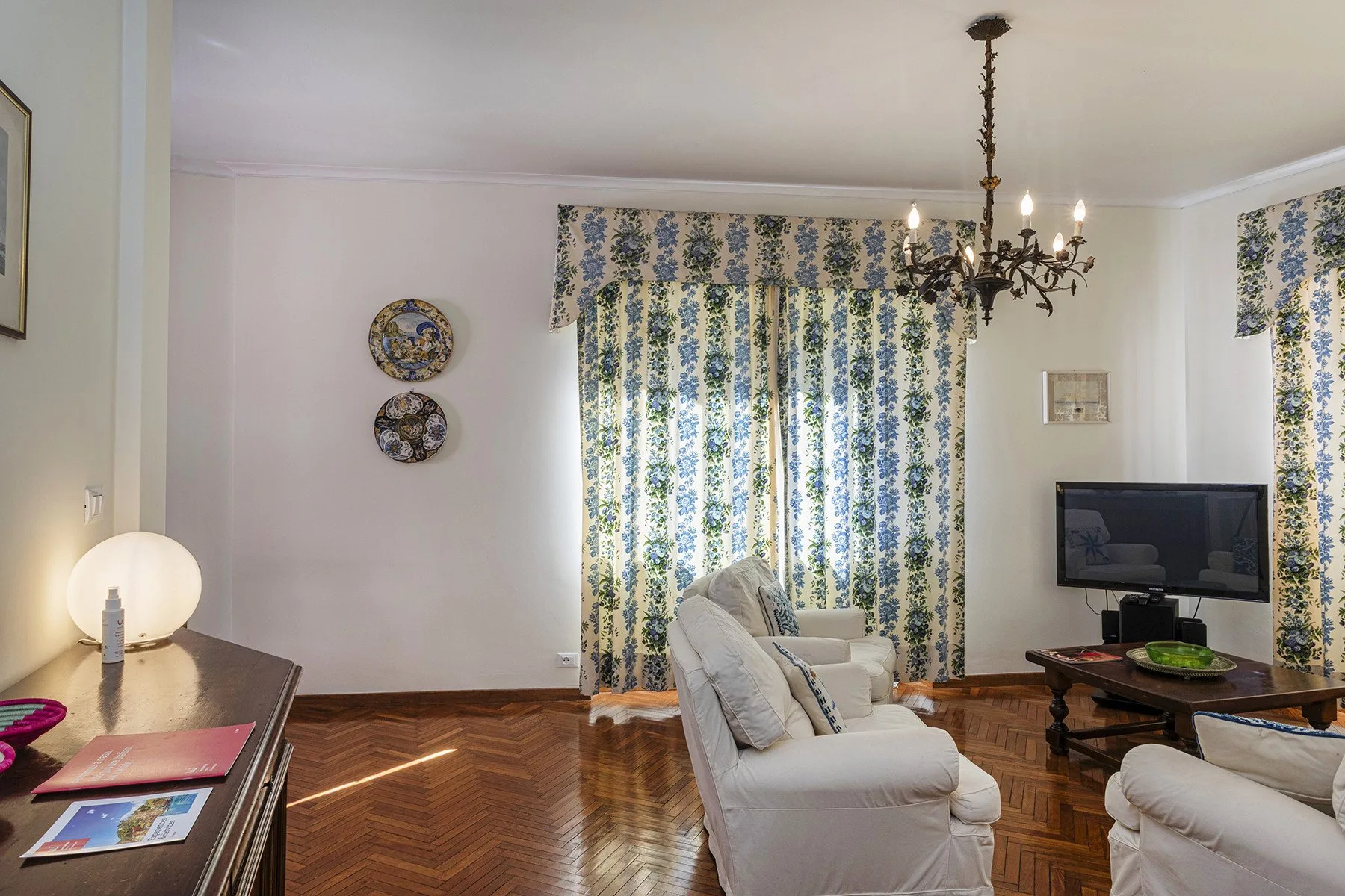 Una sala de estar con asientos tapizados, cortinas estampadas y un televisor.
