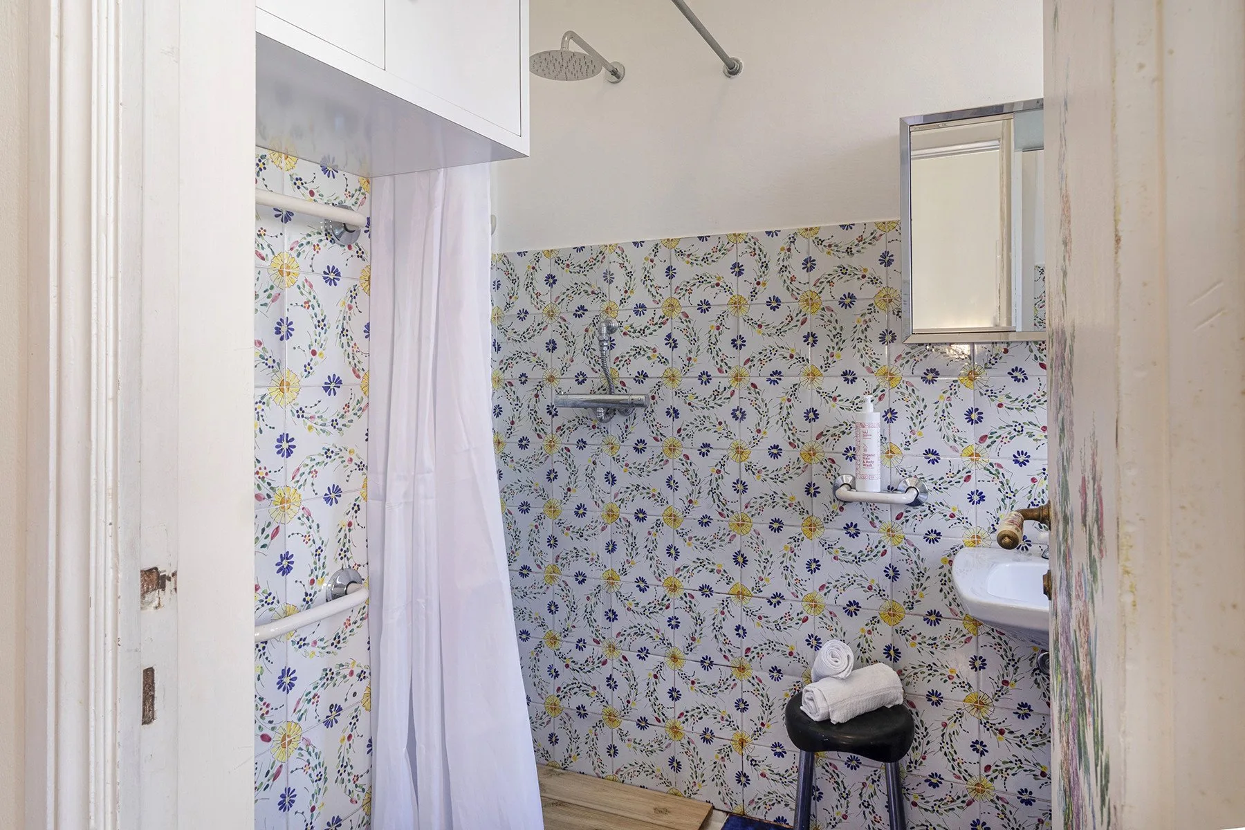 Un baño con azulejos estampados, una ducha y un lavabo pequeño.