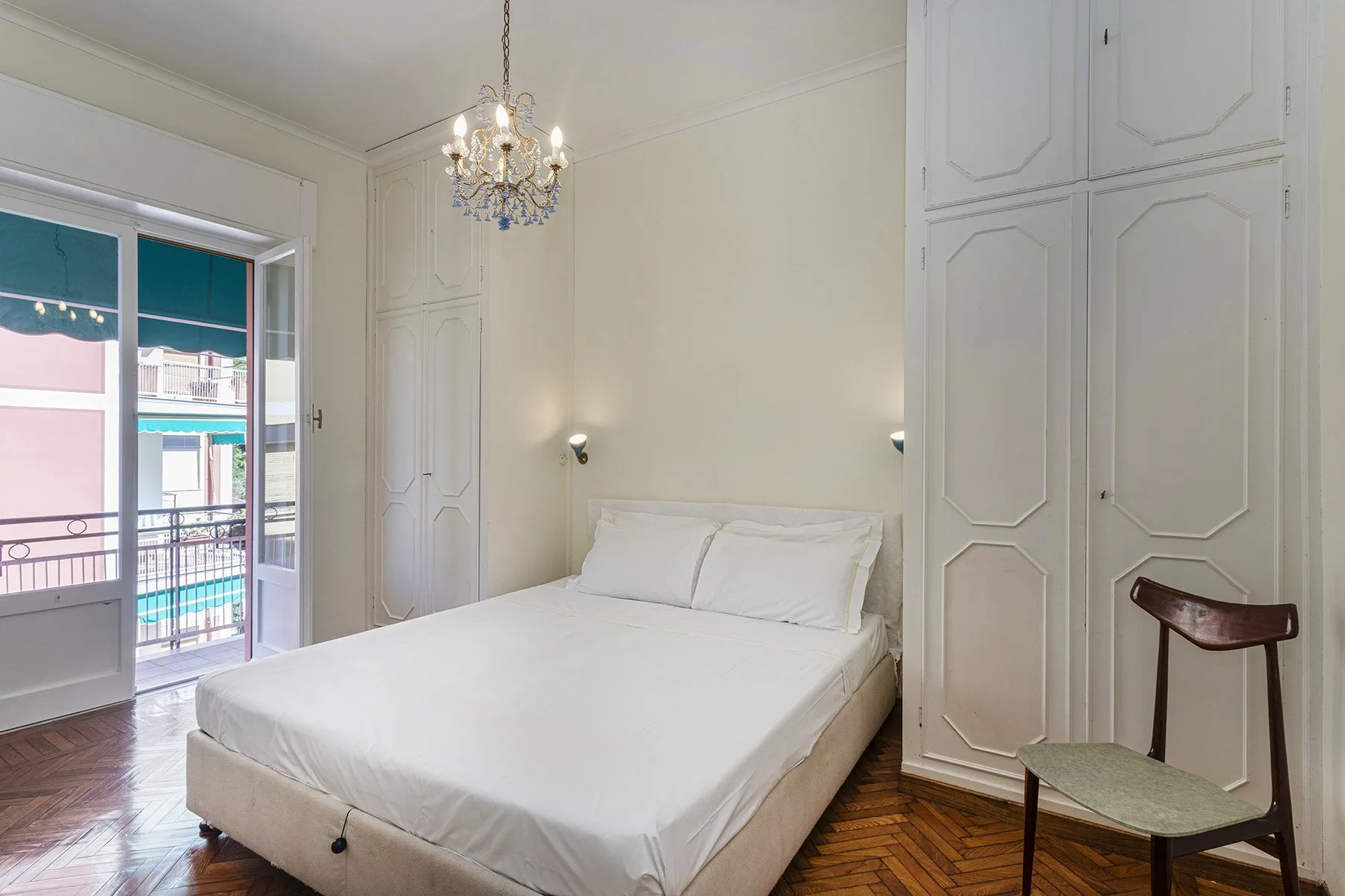 Un dormitorio luminoso con una cama, armarios con paneles y una puerta de cristal al balcón.