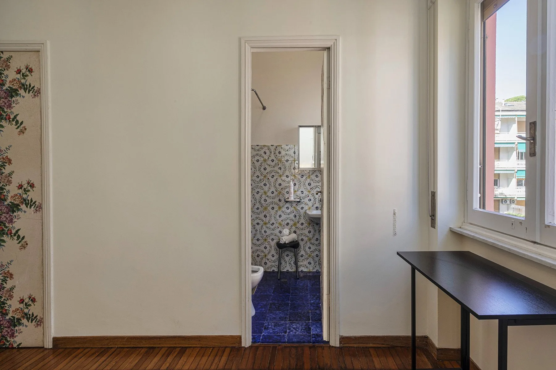 Una puerta da a un baño con azulejos estampados en las paredes y suelo azul oscuro.