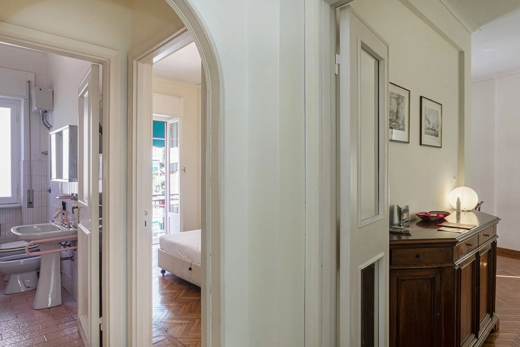 Un pasillo interior luminoso da a un baño y un dormitorio, con una cómoda cerca.