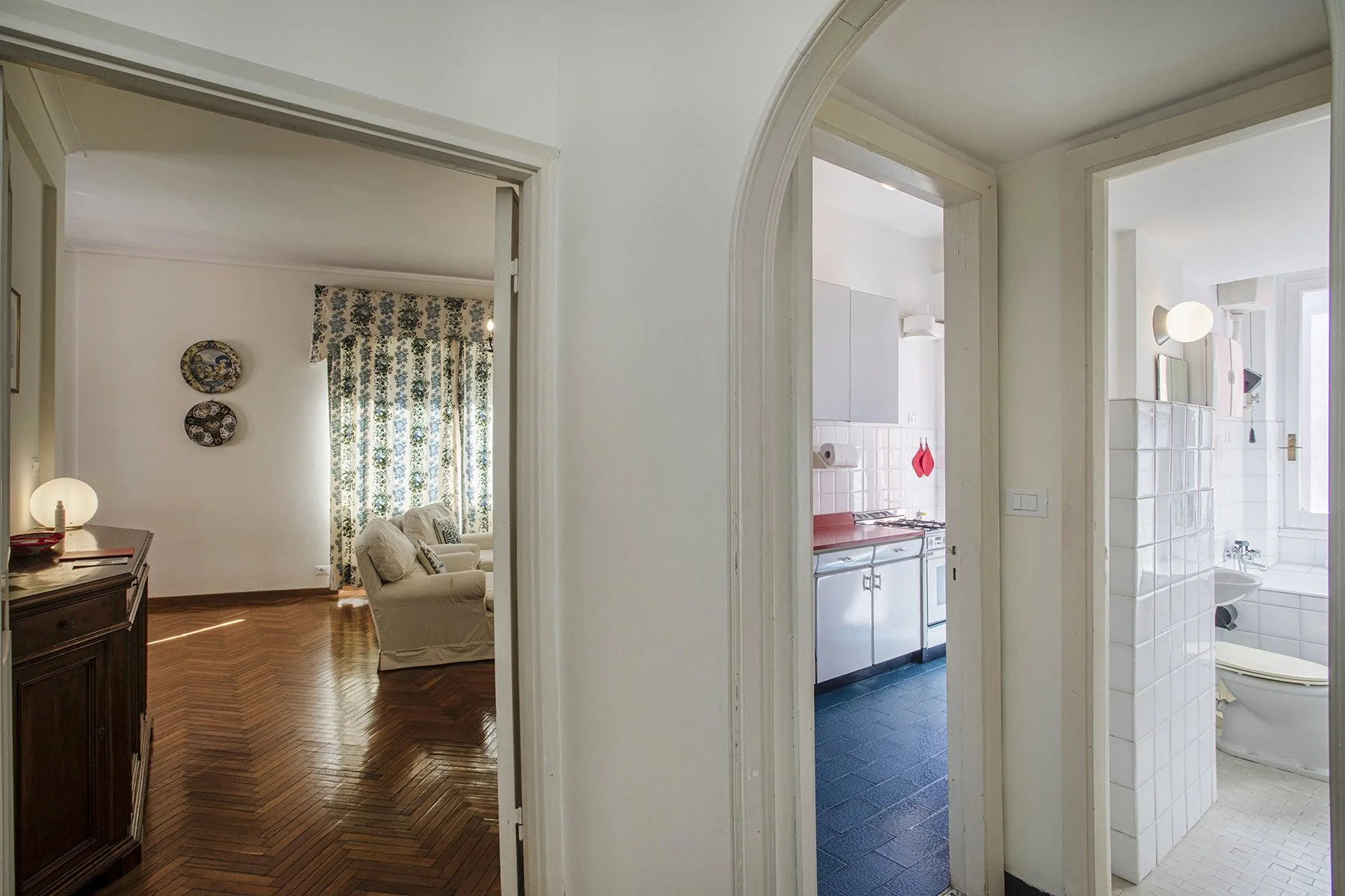 Pasillo interior con puertas abiertas que dan a una sala, una cocina y un baño.