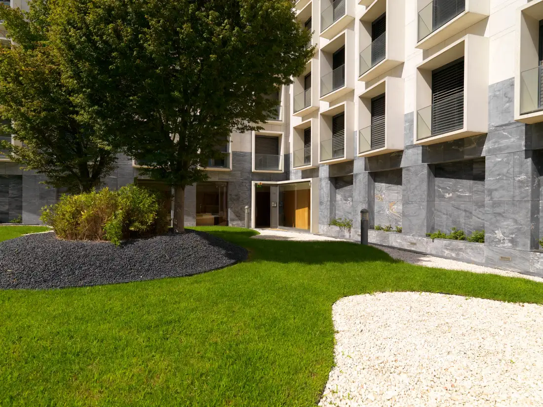 An apartment building borders a landscaped courtyard with green lawn and shrubs.