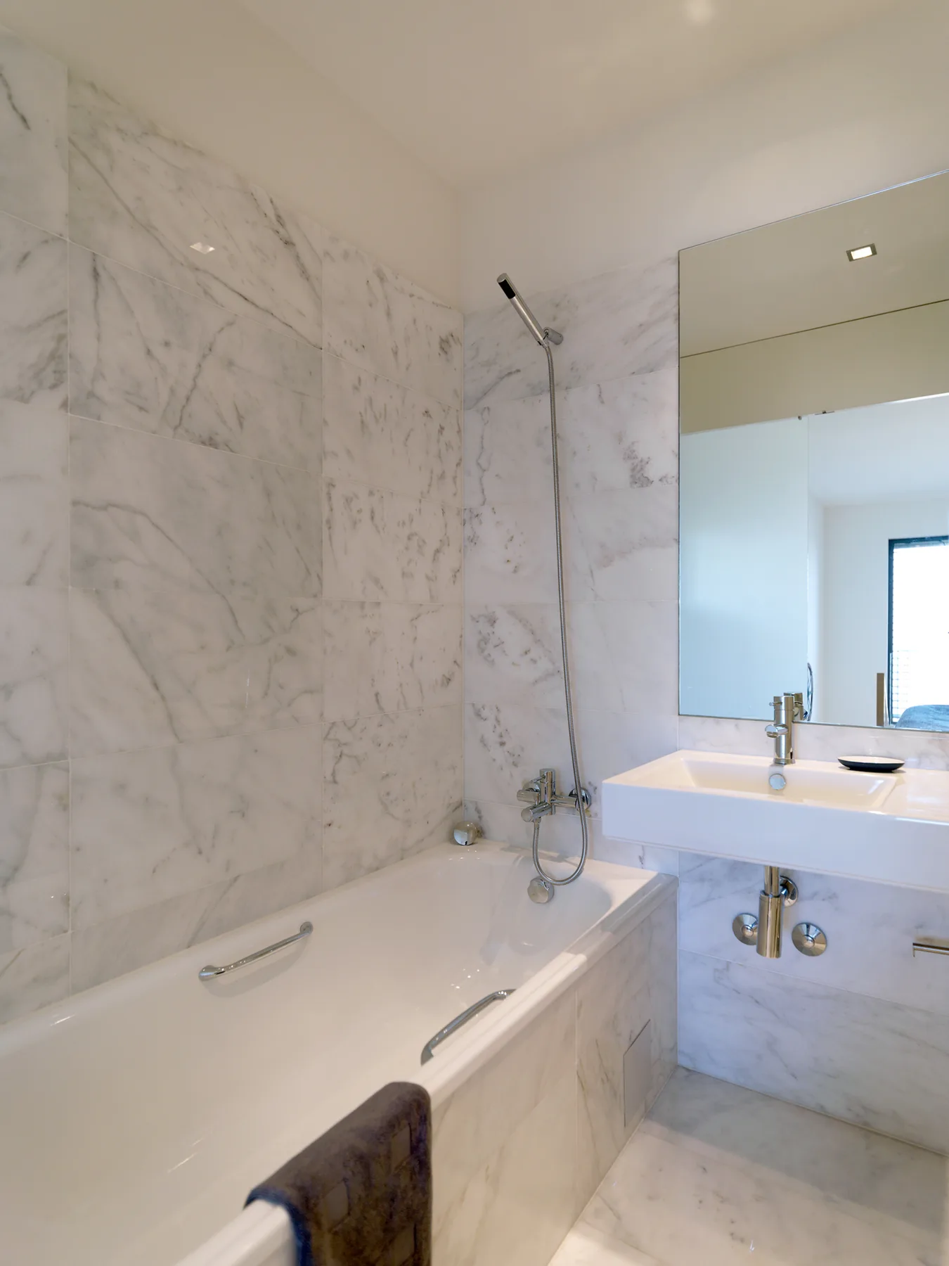 A marble bathroom with a bathtub, handheld shower, and sink.