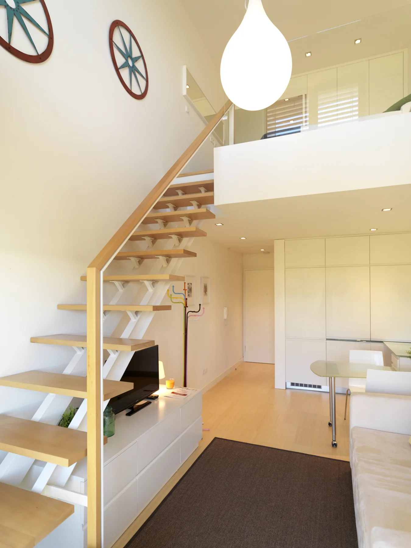 A bright loft living area features an open staircase and a dining table.