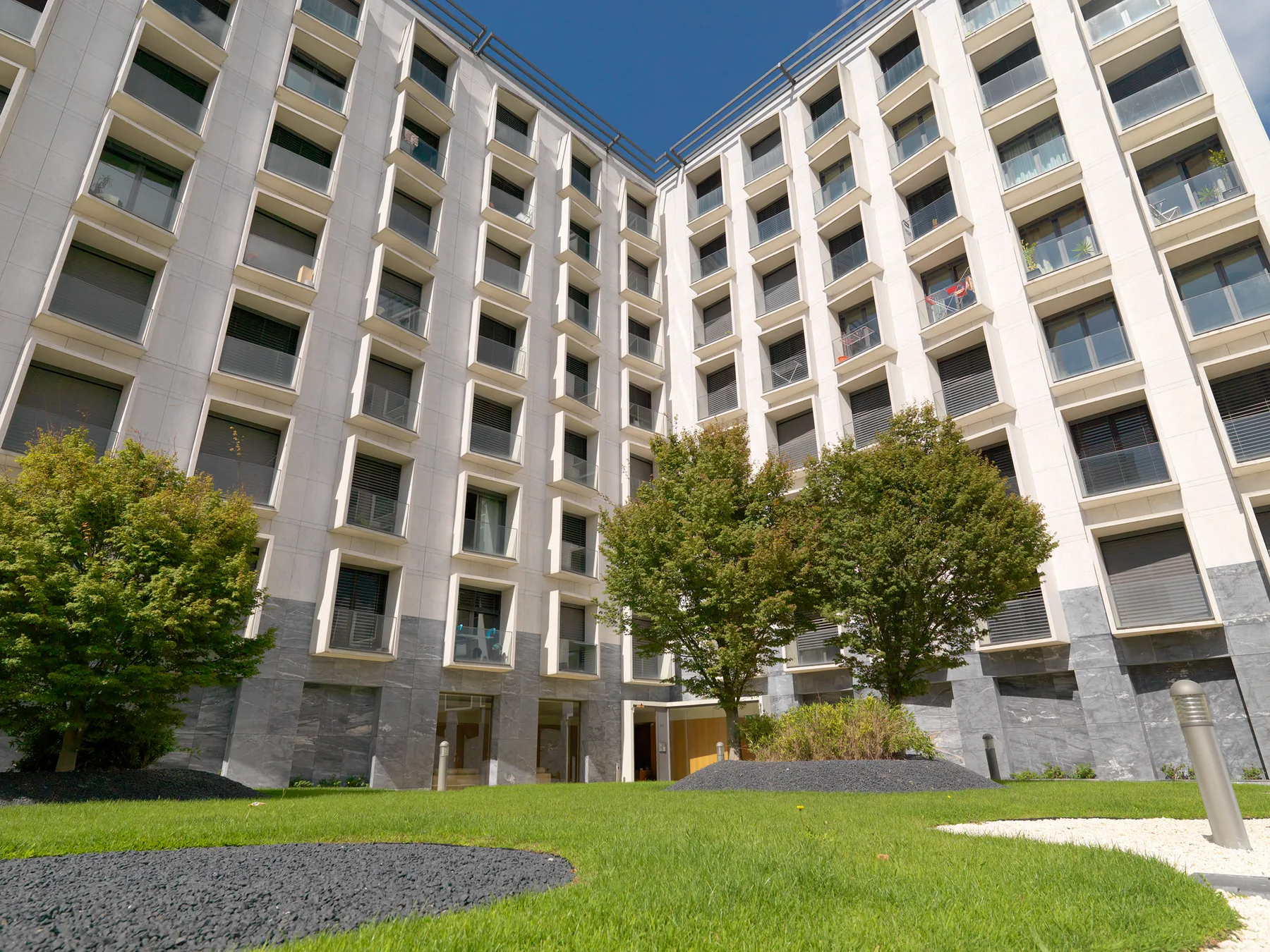 A multi-story apartment building surrounds a courtyard with grass and trees.