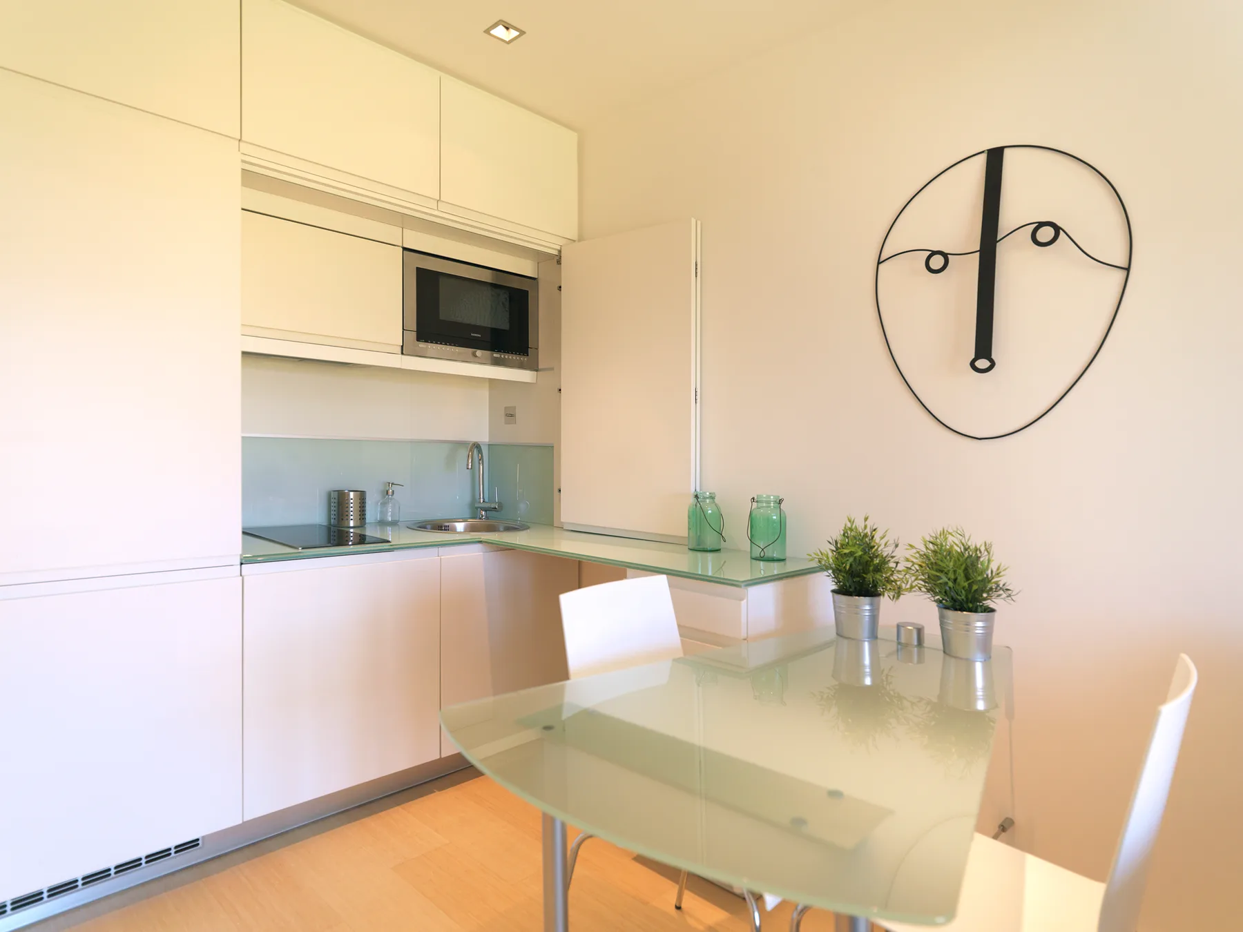 A bright kitchen and dining area with a glass table and wall clock.