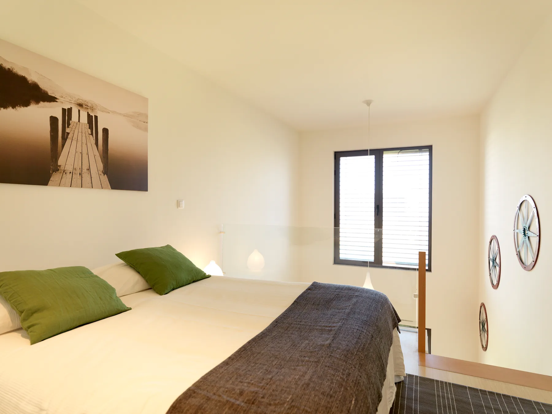 A bright bedroom with a bed, green pillows, and a window.