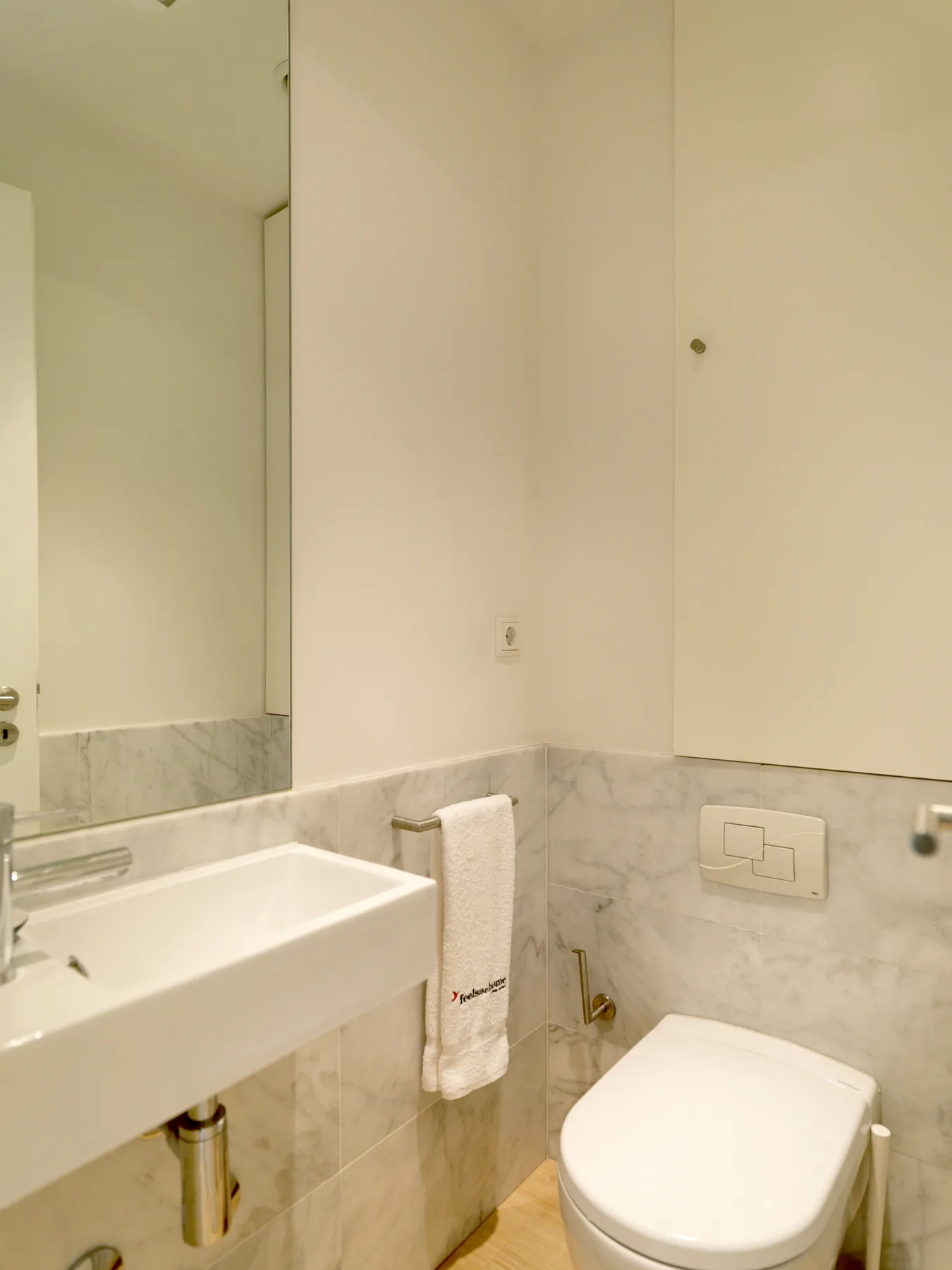 A bathroom with a sink, toilet, and wall-mounted flush plate.
