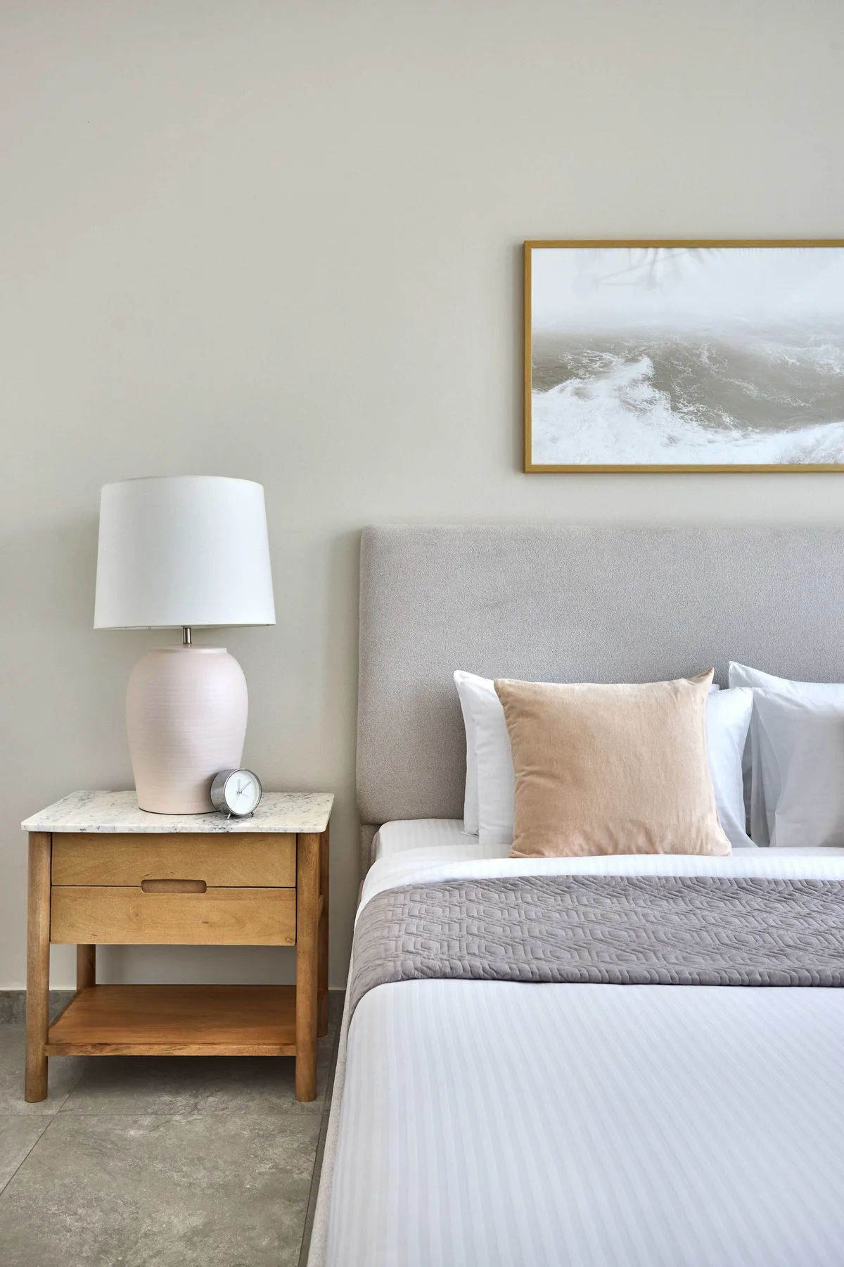 A bedroom with a bed, bedside table, and framed landscape artwork.