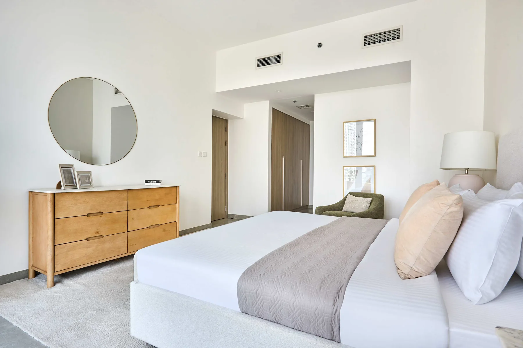 A bright bedroom with a bed, wooden dresser, and round wall mirror.