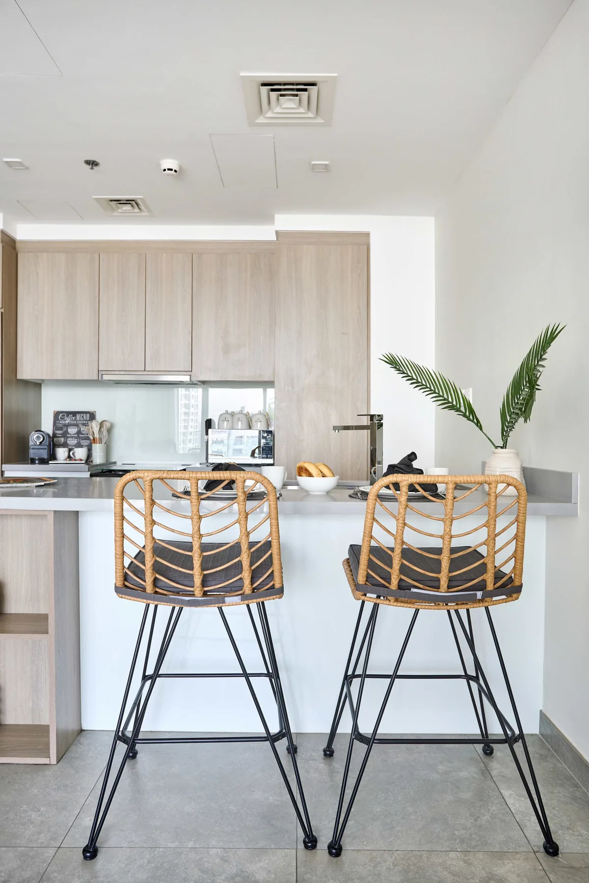 A bright kitchen with a counter, two bar stools, and a potted palm.