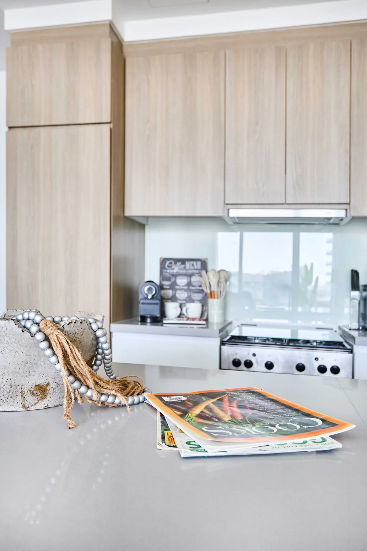 A modern kitchen with pale wood cabinets and cooking magazines on the counter.