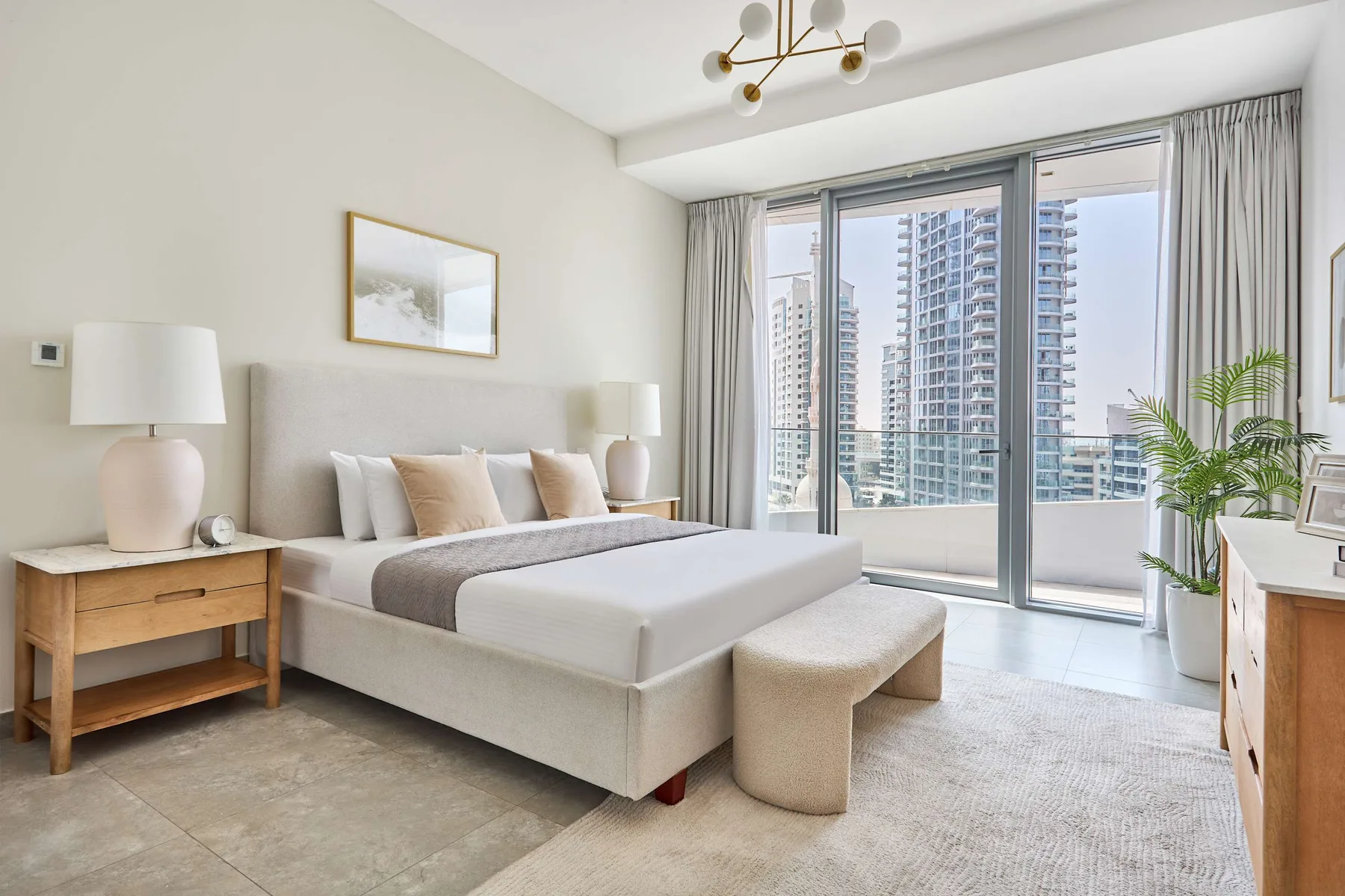 A bright bedroom with a bed, bedside tables, and large windows.