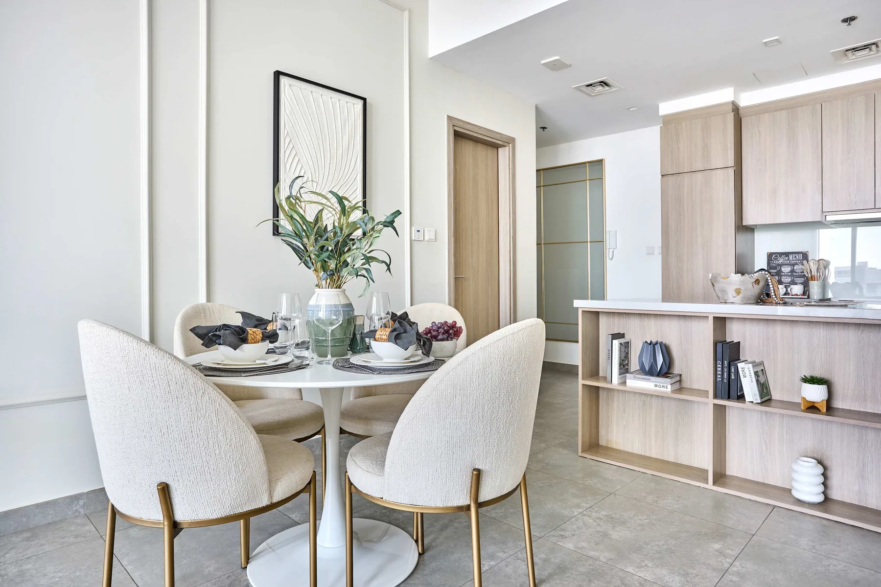 A dining area with a round table and light-colored seating beside a kitchen.