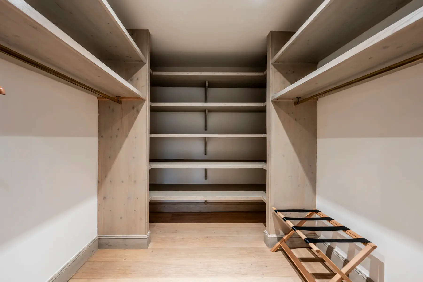 Spacious walk-in closet with wooden shelves, hanging rods, and a shoe rack on a wooden floor.