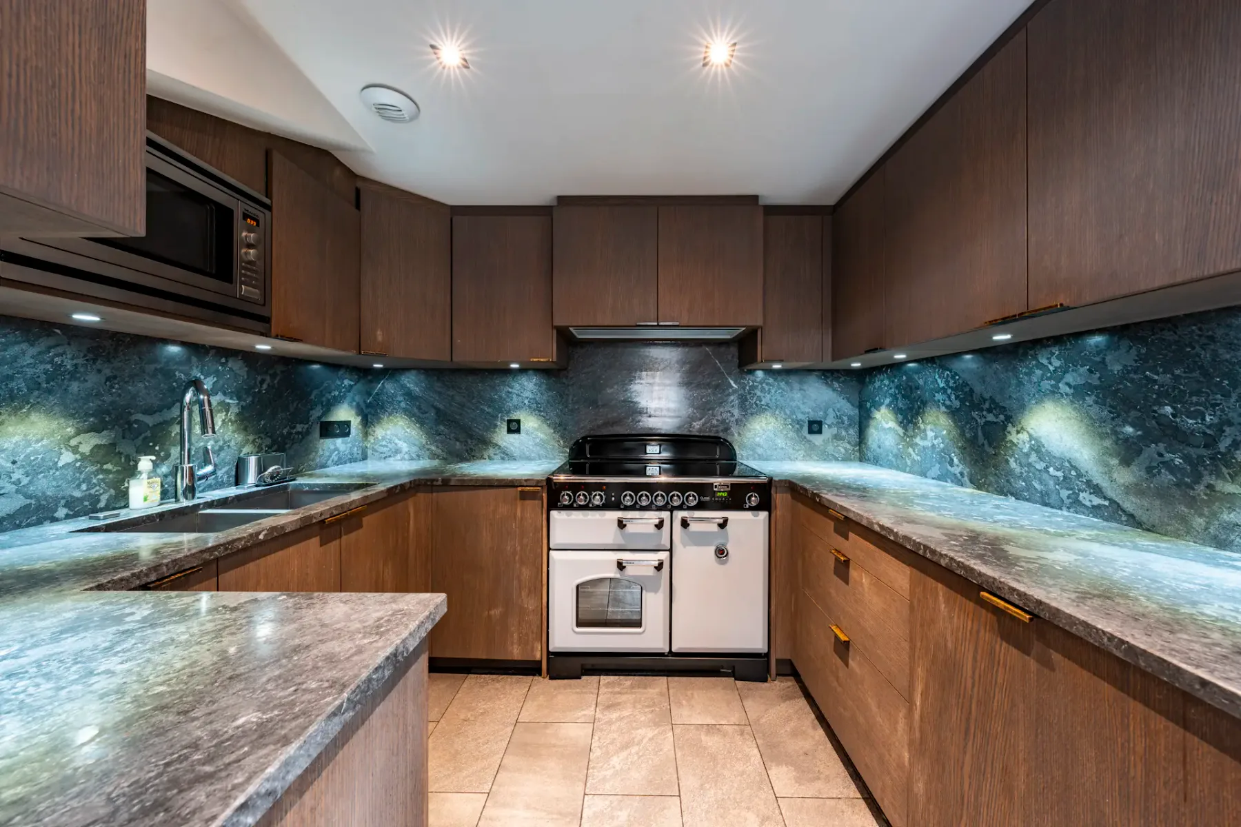 Modern kitchen with dark wood cabinets, marble countertops, a vintage-style stove, and under-cabinet lighting.