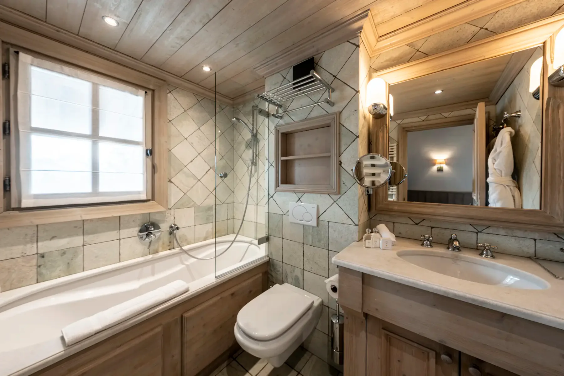 Cozy bathroom with wooden accents, featuring a bathtub, wall-mounted shower, toilet, and double sink vanity with a large mirror.